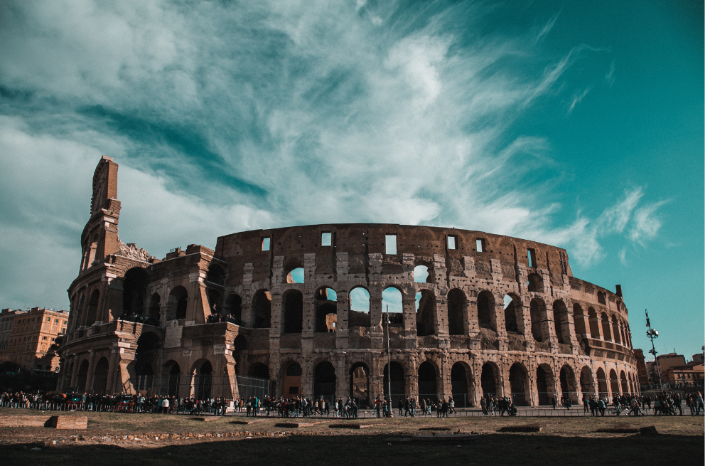 Fotografía exterior del Coliseo en una día soleado con una fila de personas enfrente, abajo a la izquierda.